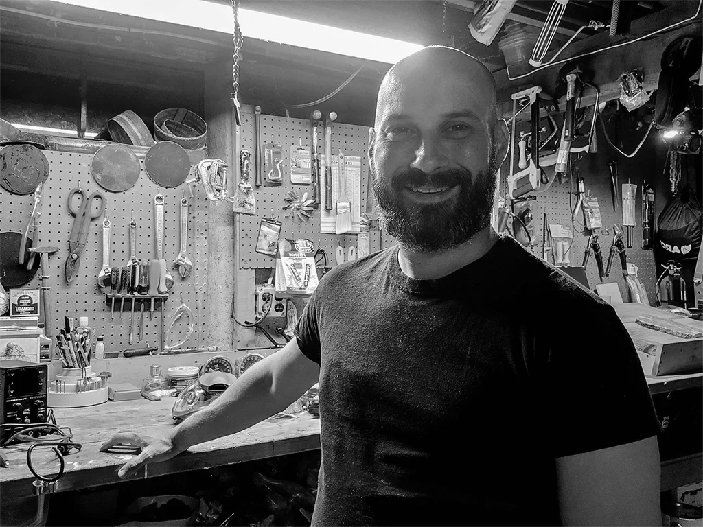 Mark from TestTalkHQ at a workshop bench with pegboard tools on the wall behind him.